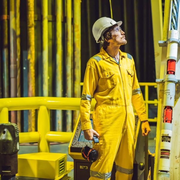 Young man in a yellow work uniform, glasses and helmet in industrial environment,oil Platform or liquefied gas plant.