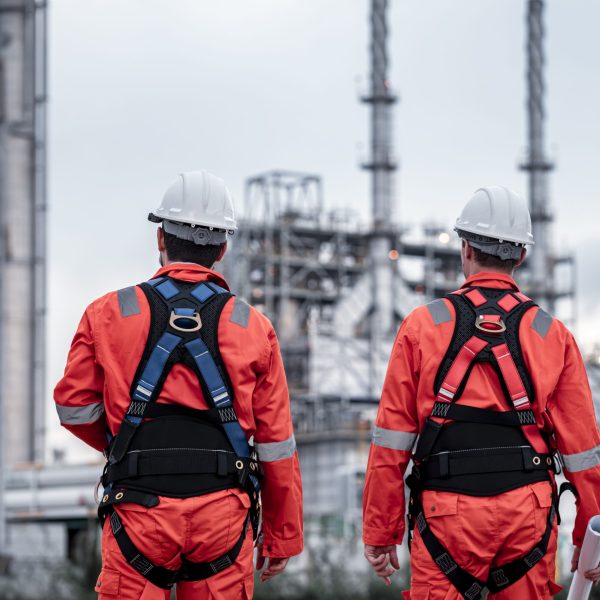 Engineer survey team wear uniform and helmet stand workplace checking blueprint project , radio communication and engineer box inspection work construction site with oil refinery background.